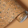 Contact paper 107: A roll of yellow terrazzo wallpaper featuring a speckled pattern in blue, white, and earthy tones, designed for modern interiors and accent walls.