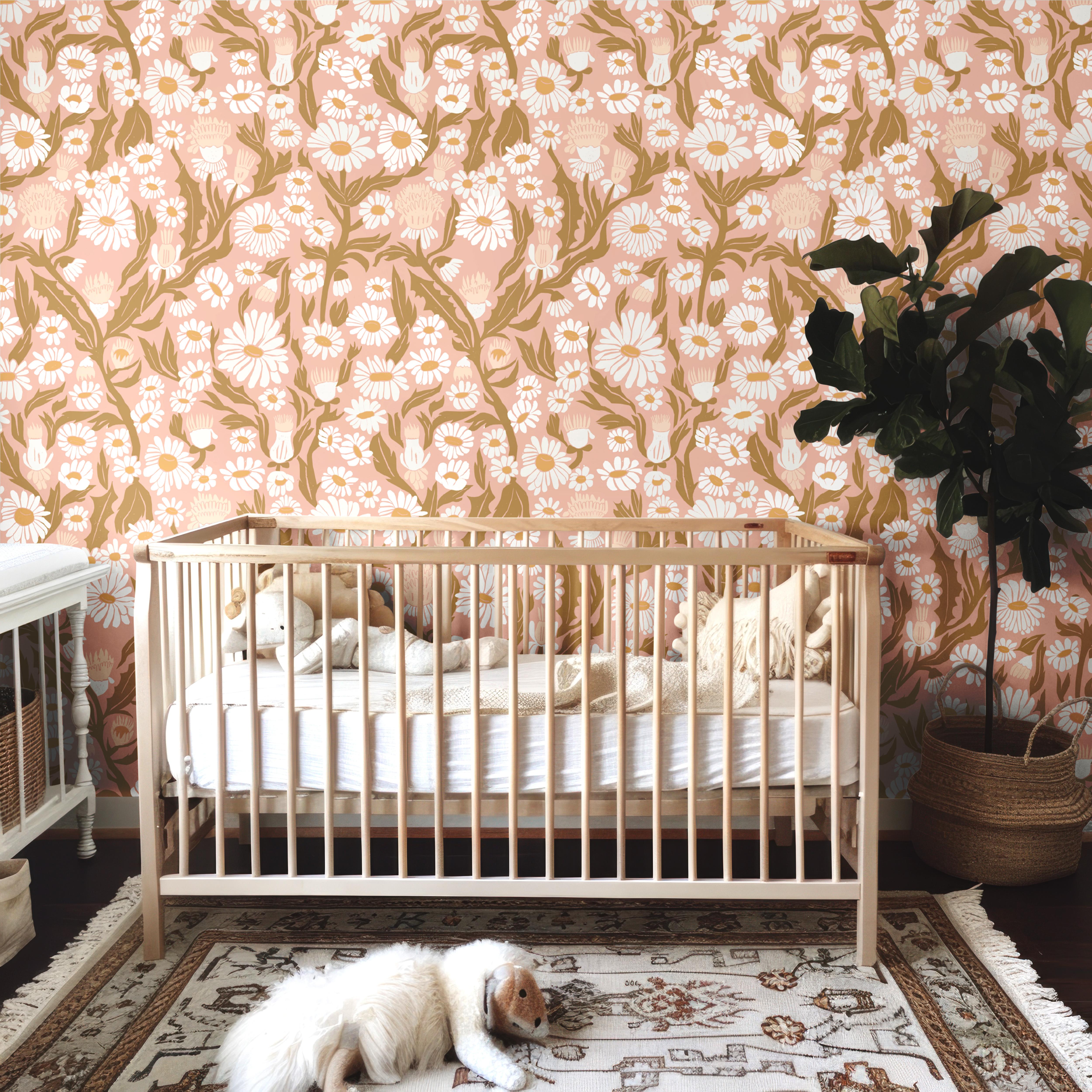 Wallpaper 1950: Blush pink floral wallpaper with white daisies and golden leafy vines featured behind a neutral wooden crib in a cozy, boho-inspired nursery.