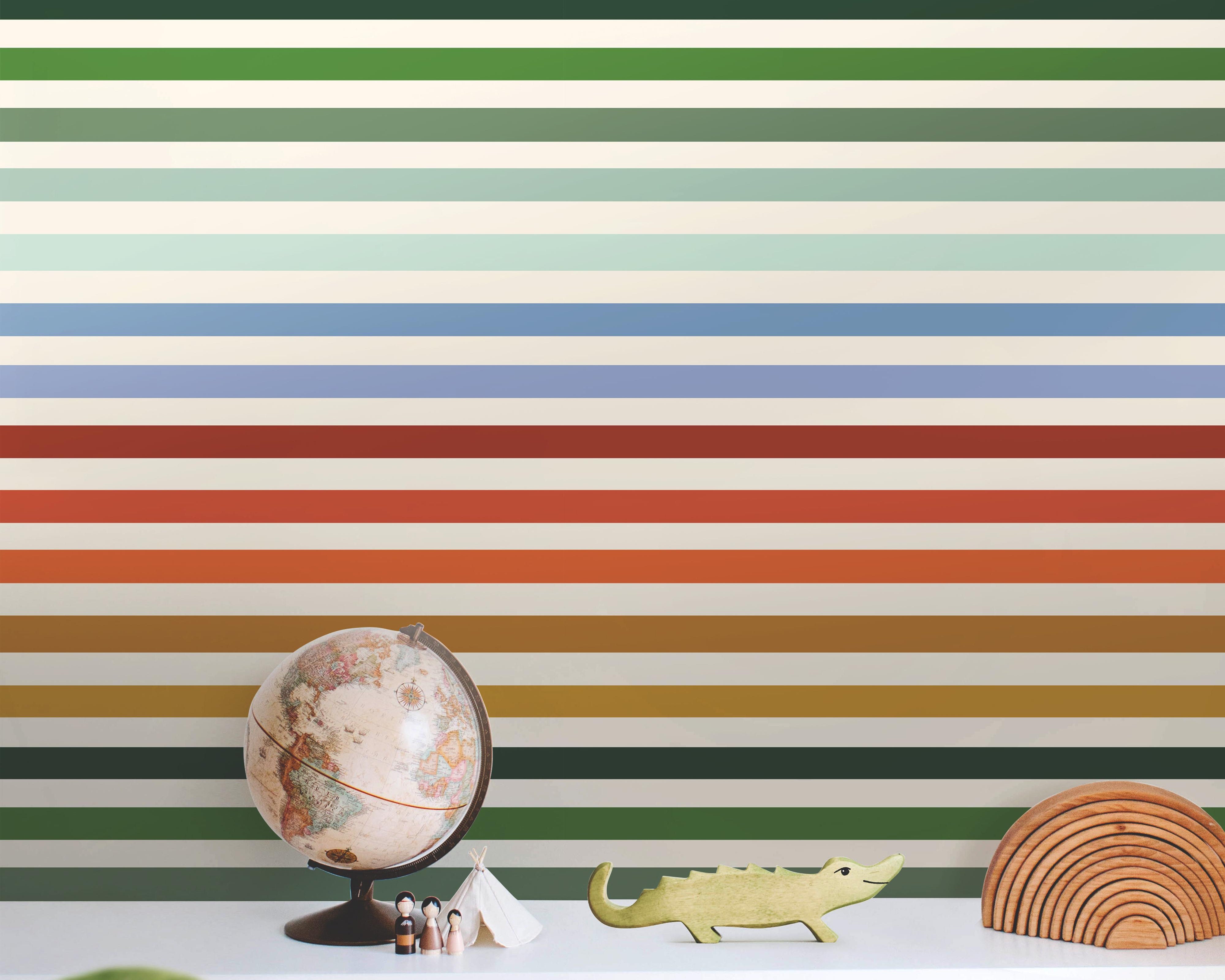 Wallpaper 1951: A playful rainbow striped wallpaper featuring bold horizontal bands in shades of orange, yellow, green, and blue, styled behind a children's shelf with toys and natural woven baskets for a cheerful, modern nursery or playroom.