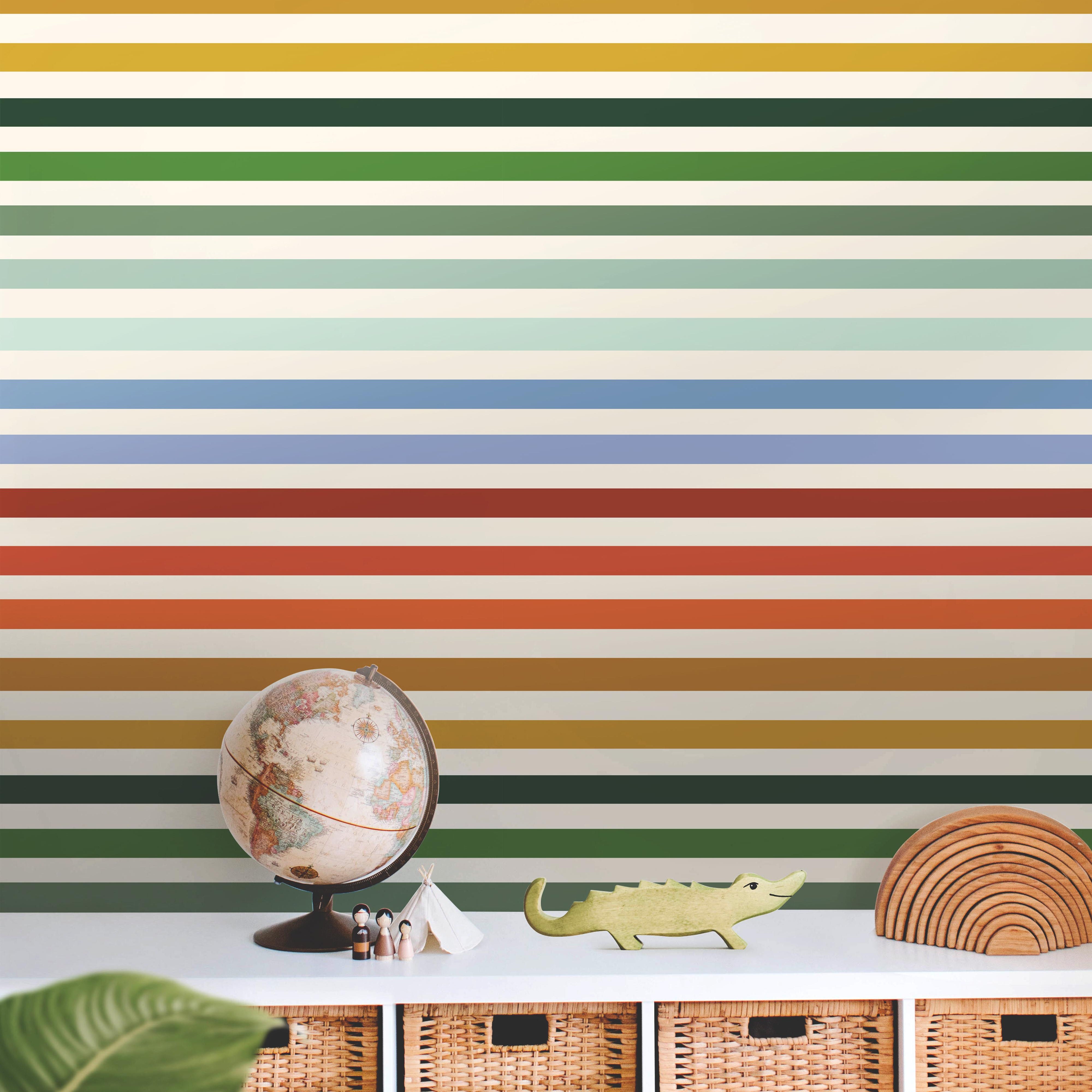 Wallpaper 1951: A playful rainbow striped wallpaper featuring bold horizontal bands in shades of orange, yellow, green, and blue, styled behind a children's shelf with toys and natural woven baskets for a cheerful, modern nursery or playroom.