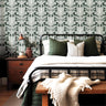 Wallpaper 1956: Vintage-inspired bedroom featuring a forest green botanical wallpaper with symmetrical cream floral pattern, behind a black iron bed and earthy wood nightstand.