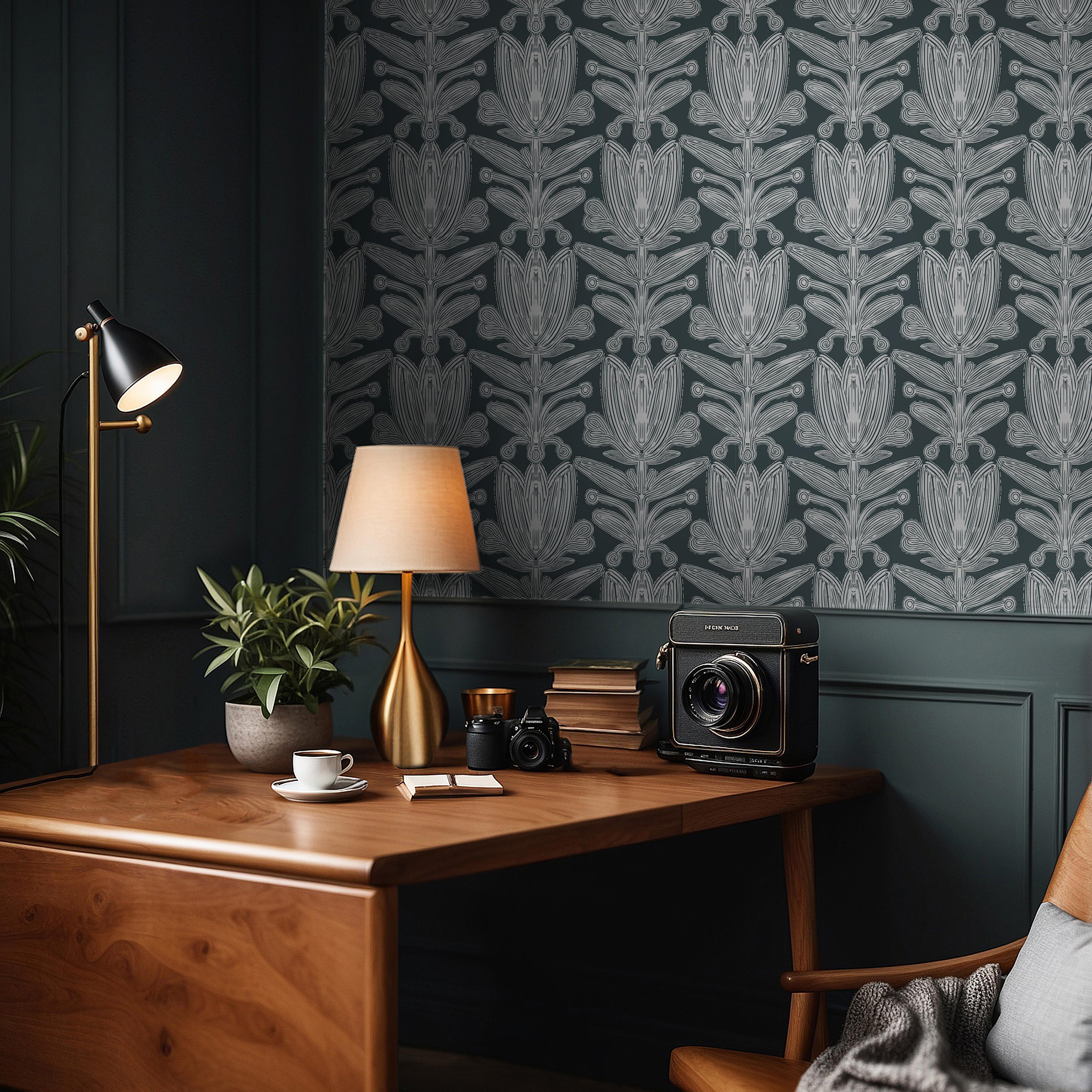 Wallpaper 1963: Dark botanical wallpaper in teal and white tones displayed behind a wooden desk with books, cameras, and a gold table lamp in a sophisticated home office.