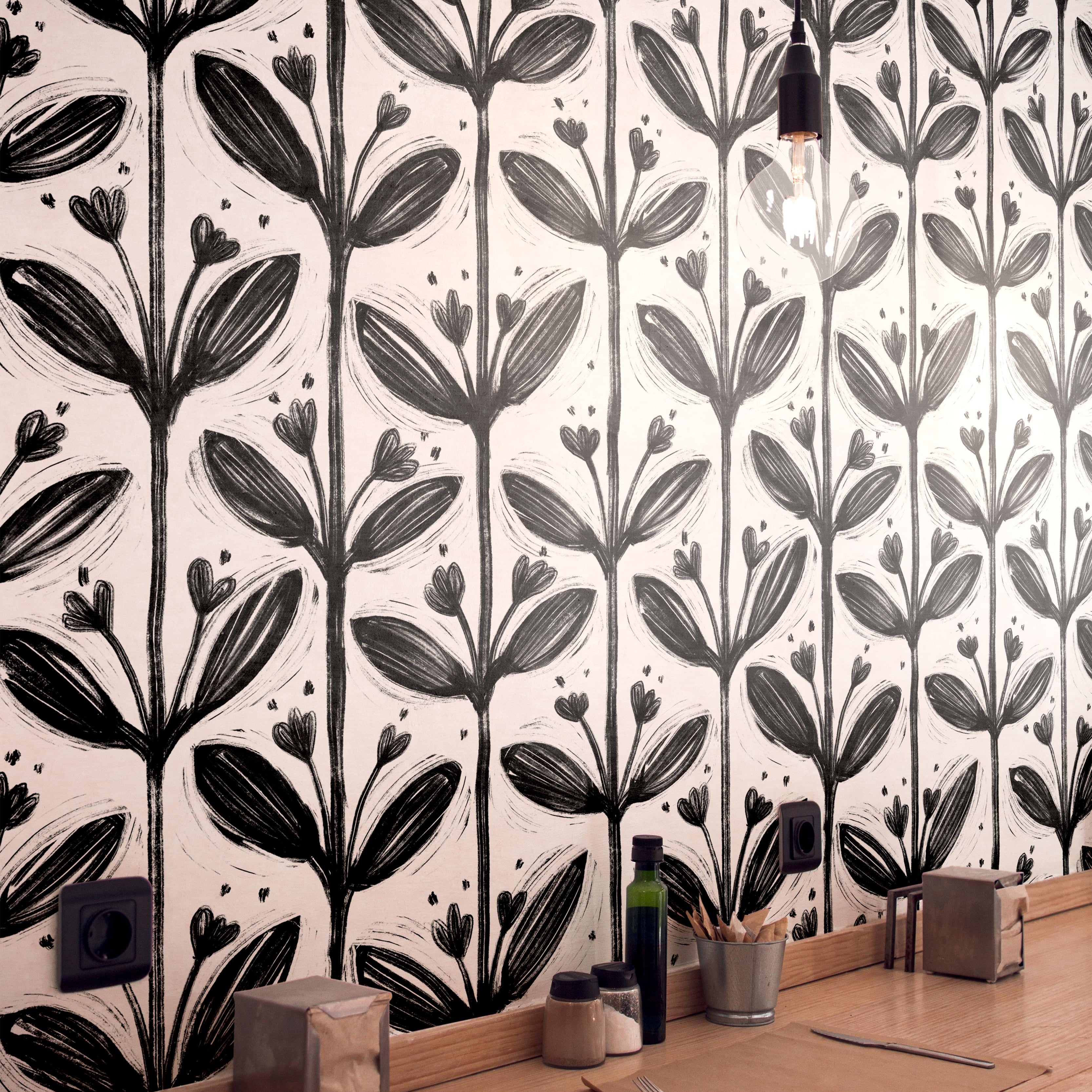 Wallpaper 1982: Modern café interior with black and white bold floral wallpaper featuring large brushstroke flowers, behind a light wood countertop with simple dining setup.

