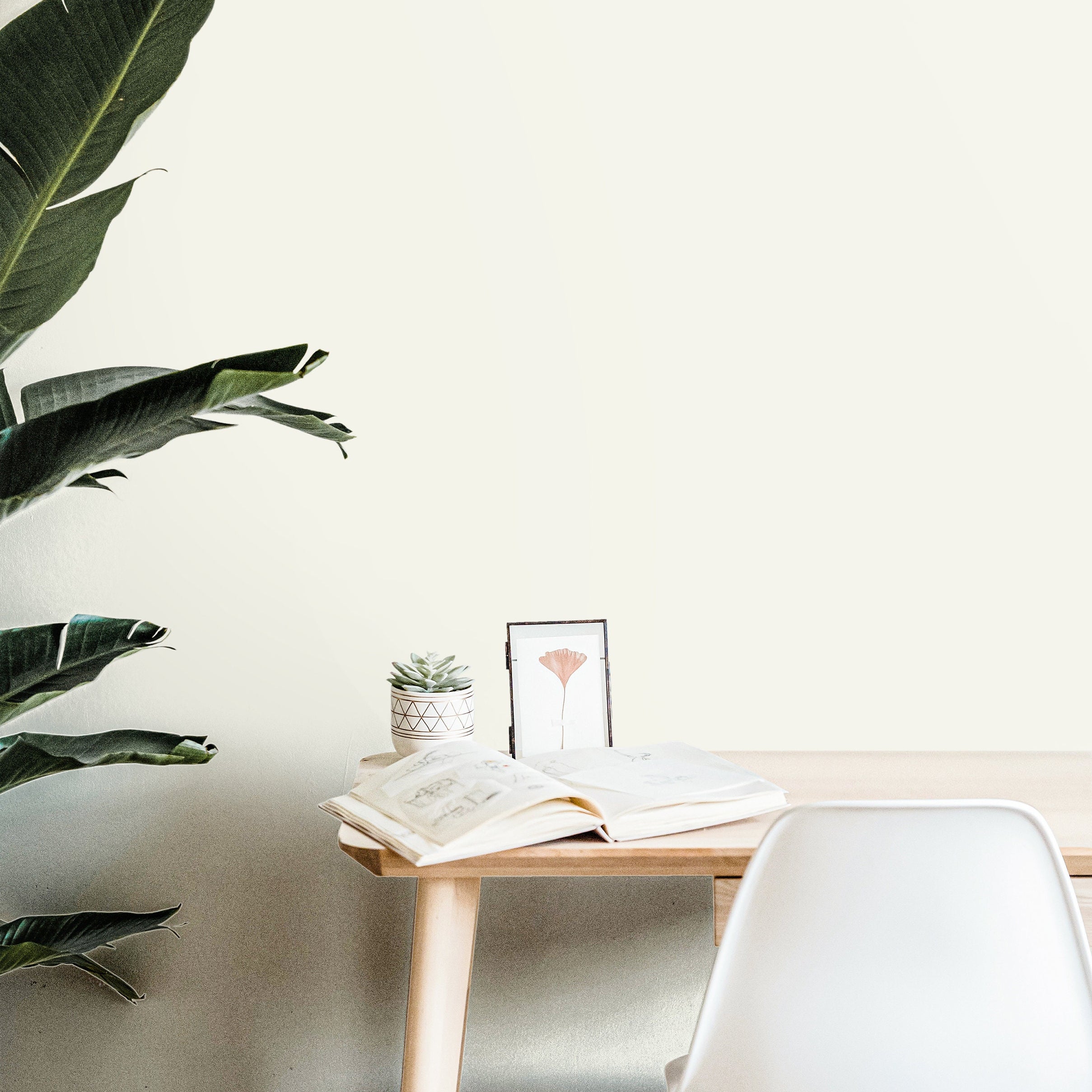 Ivory House solid cream wallpaper in a bright minimalist home office with natural wood furniture and green plants.