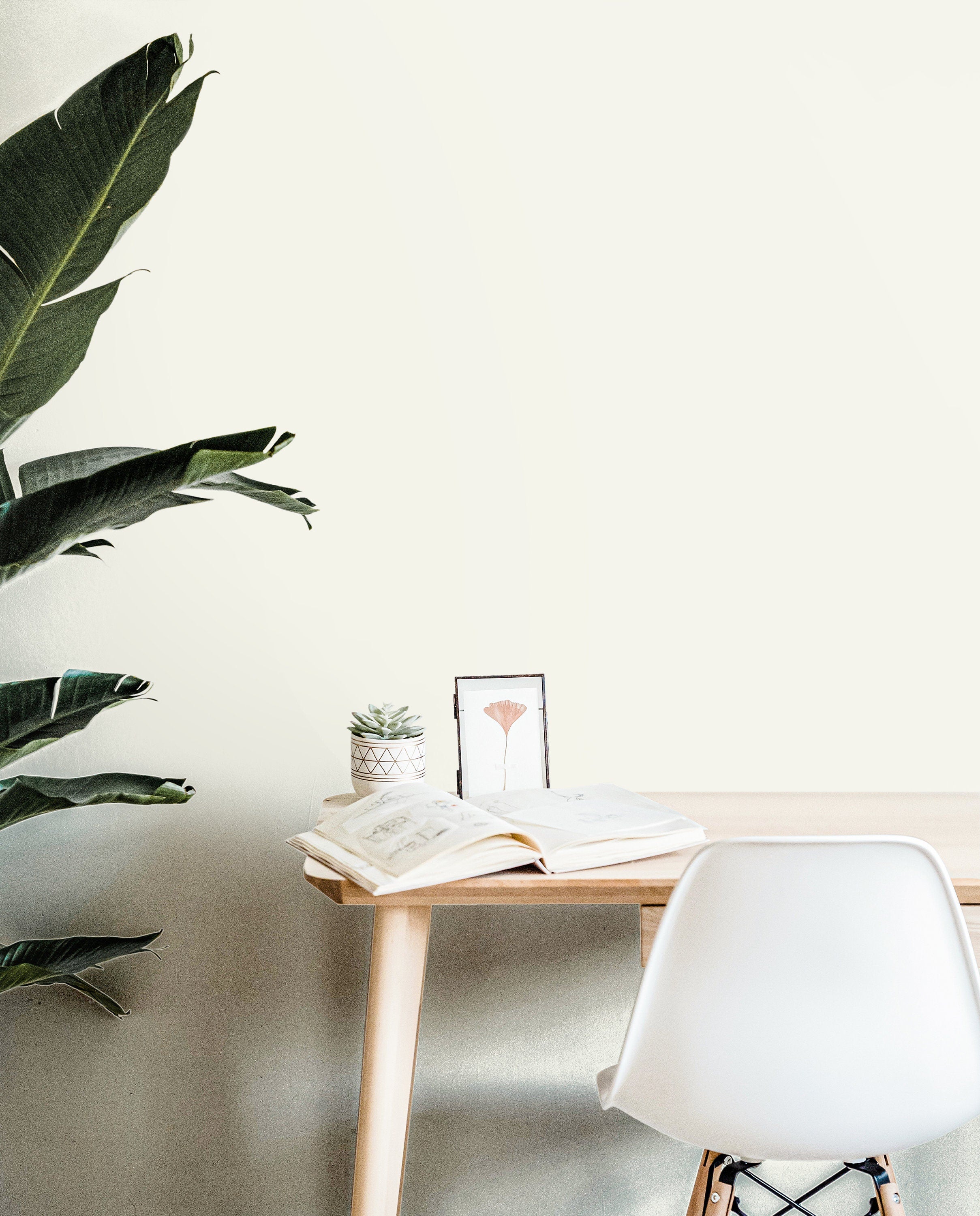 Ivory House solid cream wallpaper in a bright minimalist home office with natural wood furniture and green plants.