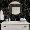 Blackmoor black floral wallpaper in a modern bathroom with a white vanity, brass mirror, and botanical décor.