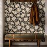 Cream florals on a black background installed in a warm entryway with dark wooden and green accents