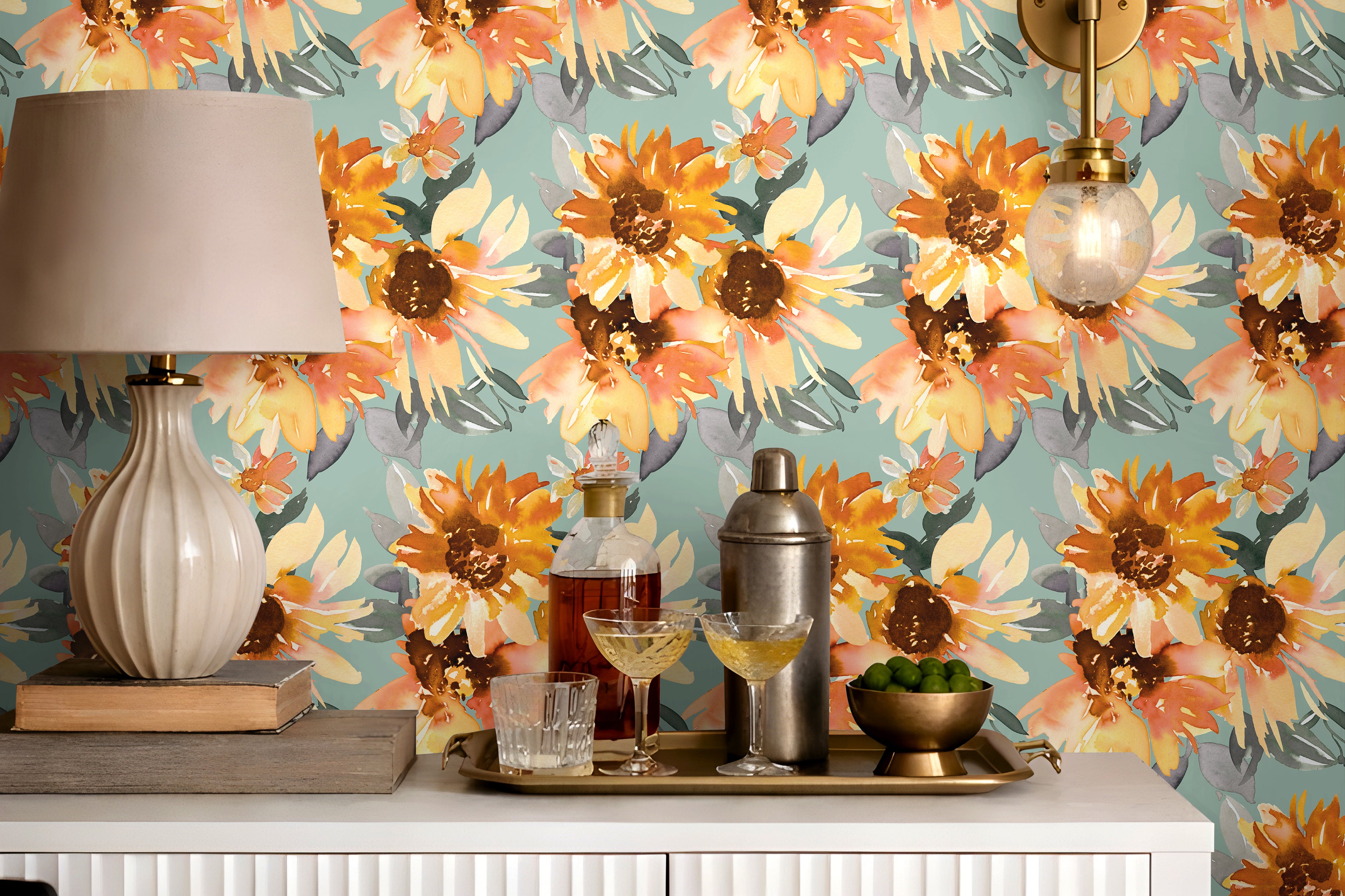 Aqua blue floral wallpaper with large orange and golden yellow sunflower blooms styled behind a white fluted bar cabinet with brass lighting and neutral decor.