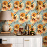 Aqua blue floral wallpaper with large orange and golden yellow sunflower blooms styled behind a white fluted bar cabinet with brass lighting and neutral decor.