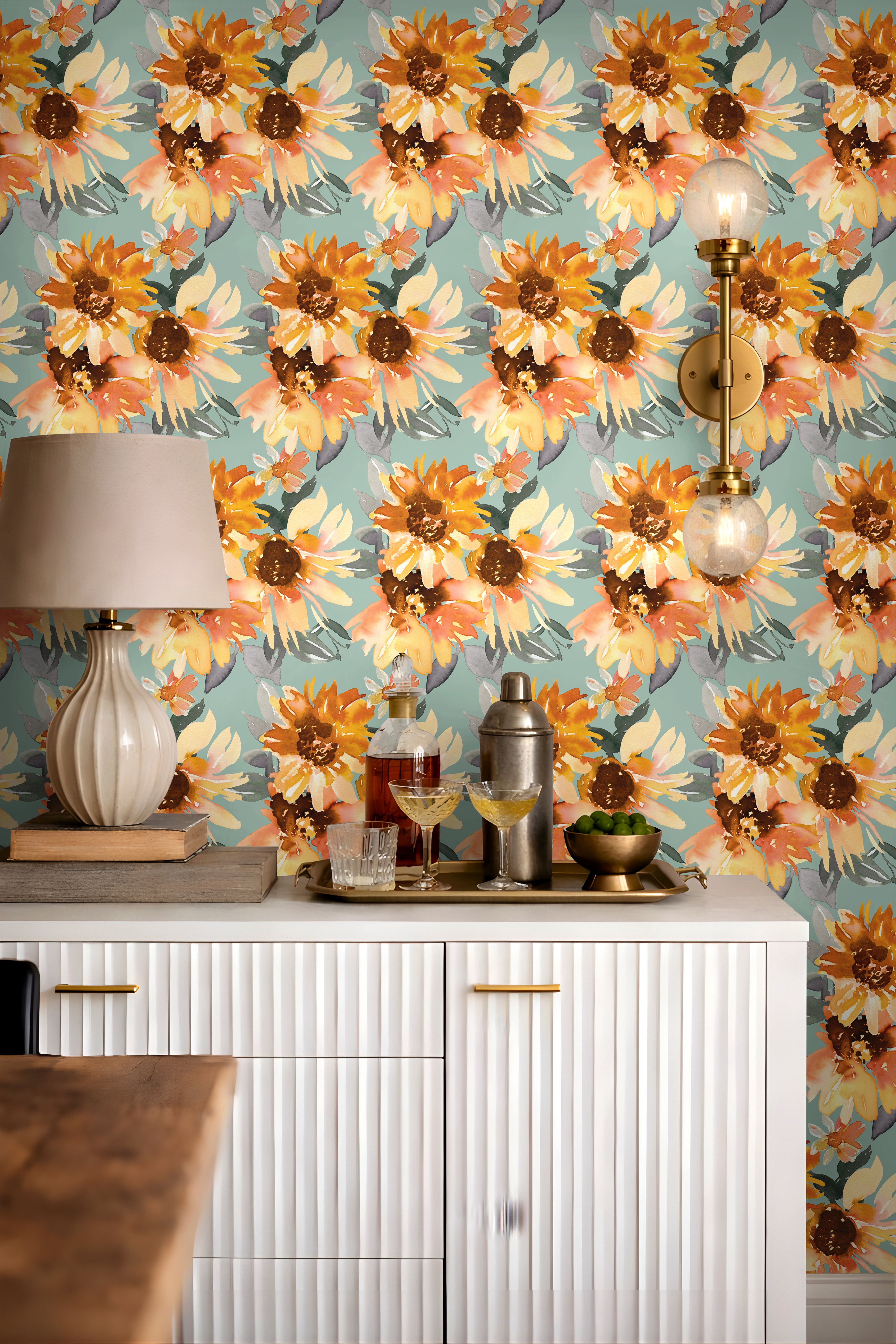 Aqua blue floral wallpaper with large orange and golden yellow sunflower blooms styled behind a white fluted bar cabinet with brass lighting and neutral decor.