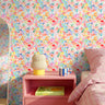 Colorful pastel floral wallpaper with painterly pink, peach, yellow, blue, and lavender flowers styled in a bright playful bedroom.
