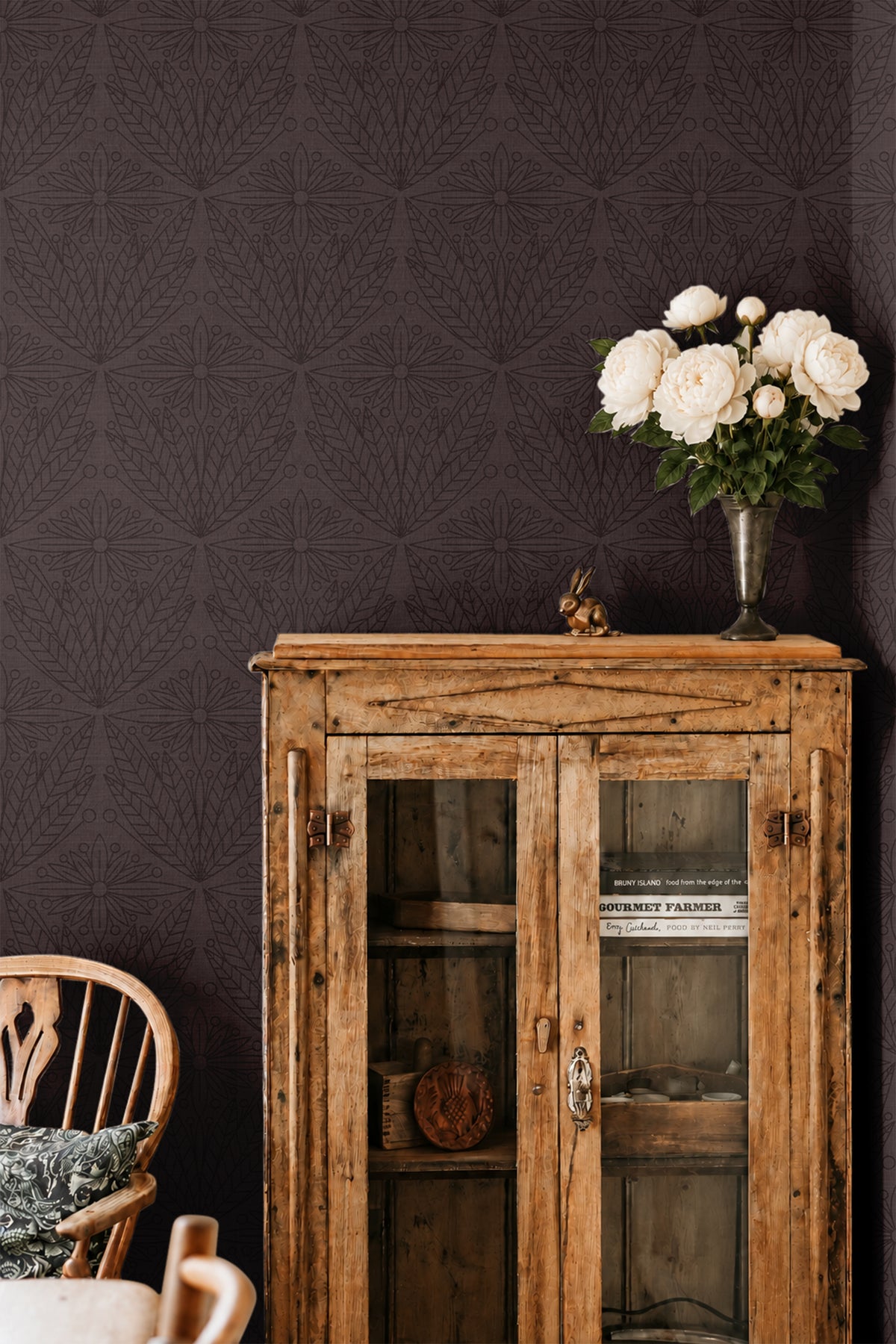 cabernet and gentry 3550 burgundy botanical wallpaper behind rustic wood cabinet with white roses in a vase and wood chair