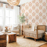 Blush botanical nursery wallpaper with watercolor coneflowers styled in a soft neutral nursery with woven textures and warm wood furniture.