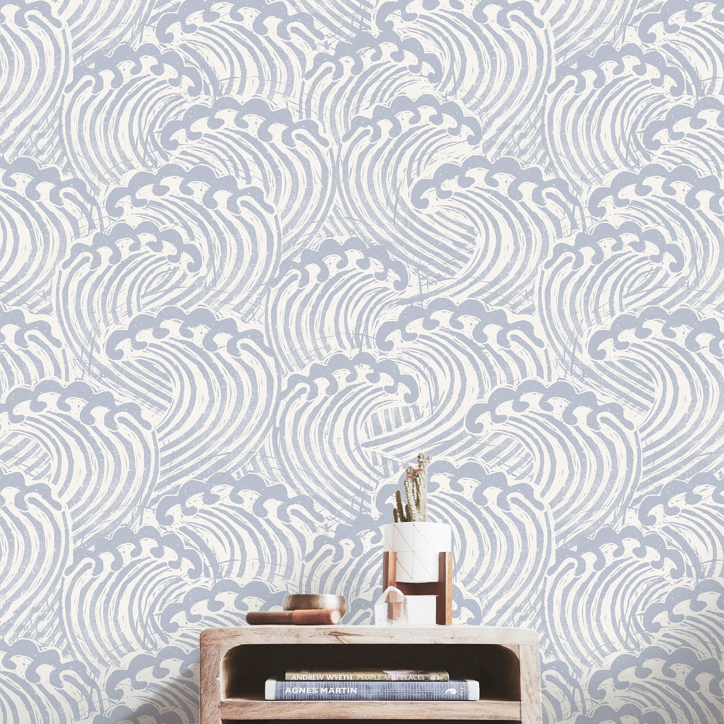 muted blue and ivory wave wallpaper behind light wood console books crystal and small planter