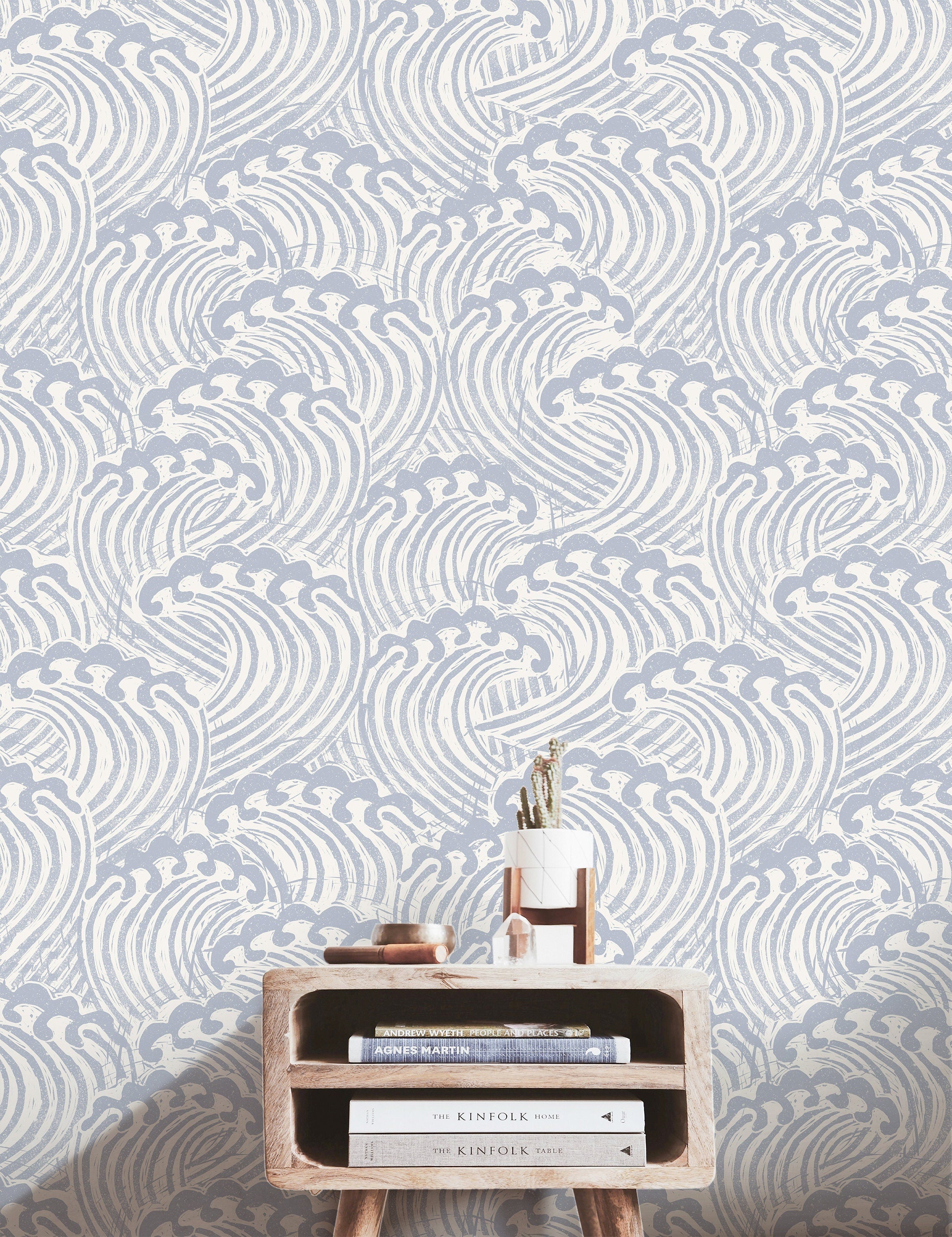 muted blue and ivory wave wallpaper behind light wood console books crystal and small planter