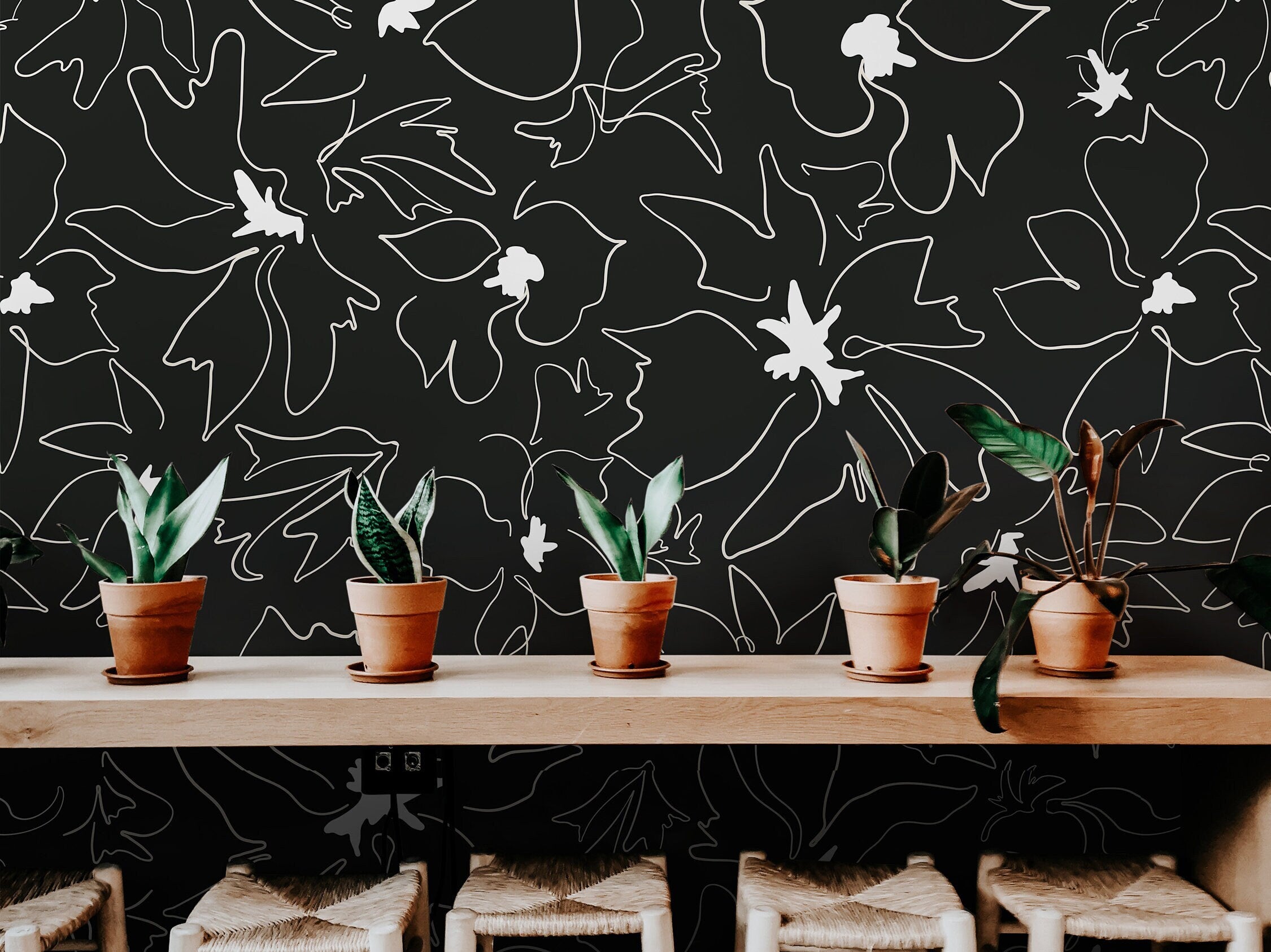 Wallpaper 1158a: Black wallpaper featuring abstract white line-drawn flowers behind a modern wood counter with potted plants and woven stools.

