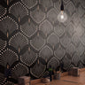 Wallpaper 1170a: Modern cafe counter with dramatic black wallpaper featuring a repeating fanburst pattern in soft beige lines, lit by a single hanging bulb.