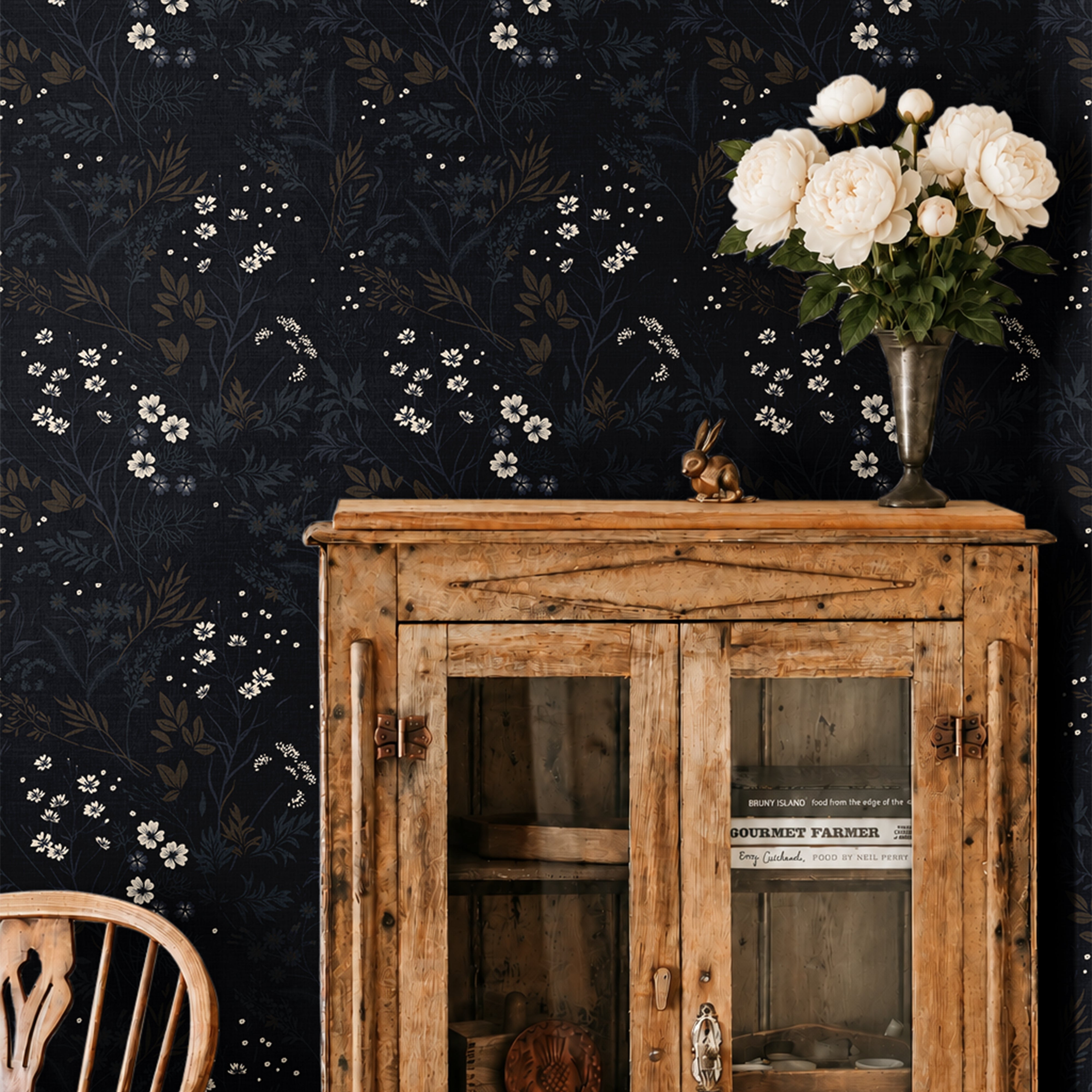 ink and elderflower 3552 moody floral wallpaper behind a rustic wood cabinet with white flowers in a vase and a wood chair