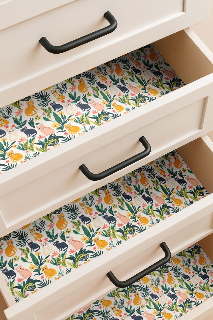 Drawer lined with playful cat and tropical leaf pattern in orange, blush, cream, and navy on a warm cream background