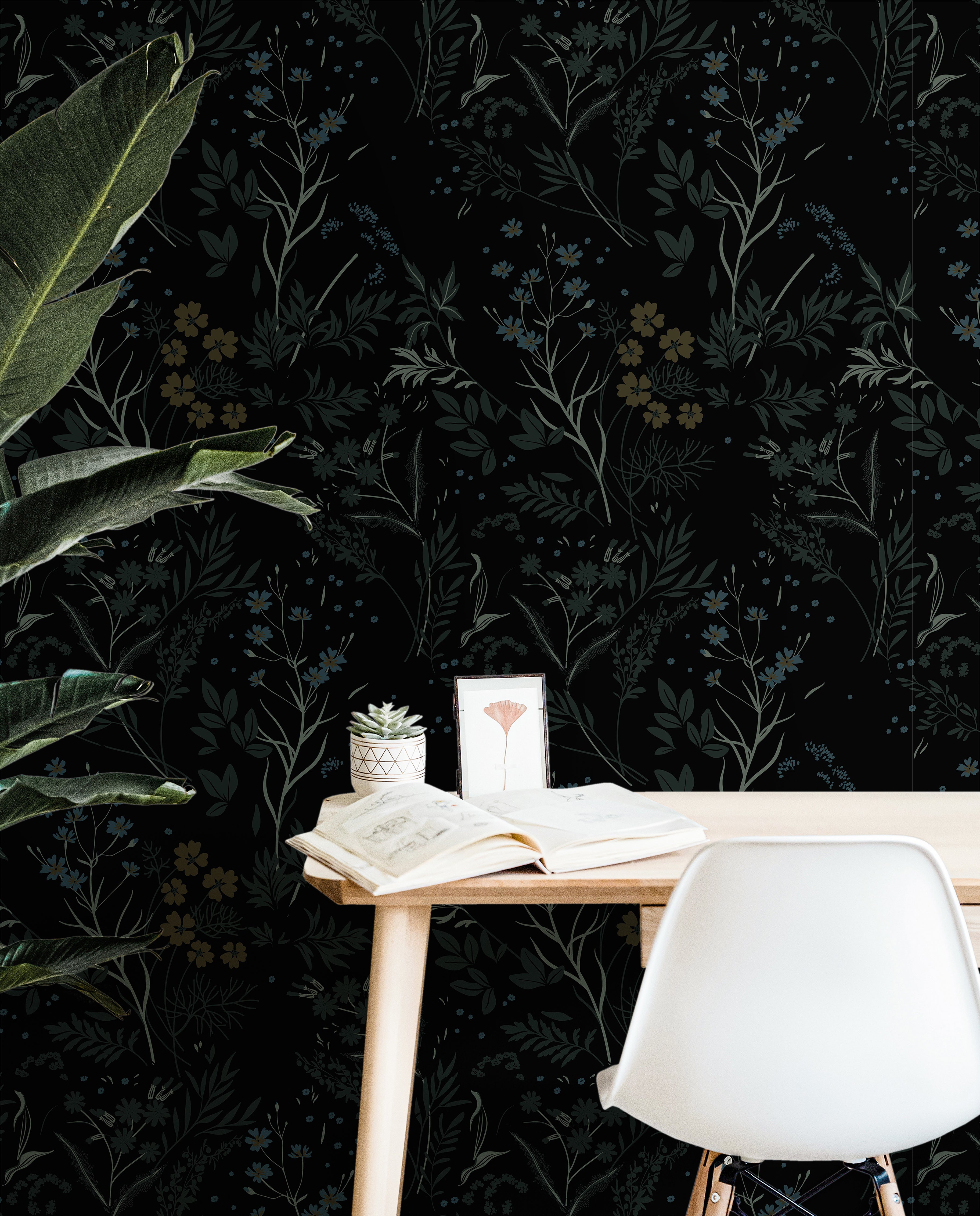 Dark botanical wallpaper featuring layered wildflowers and foliage in muted blue and green tones on a black background styled behind a modern office desk.