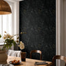 Moody black floral wallpaper with delicate blue wildflowers and olive botanical stems styled in a warm modern dining room with natural wood furniture and soft lighting.
