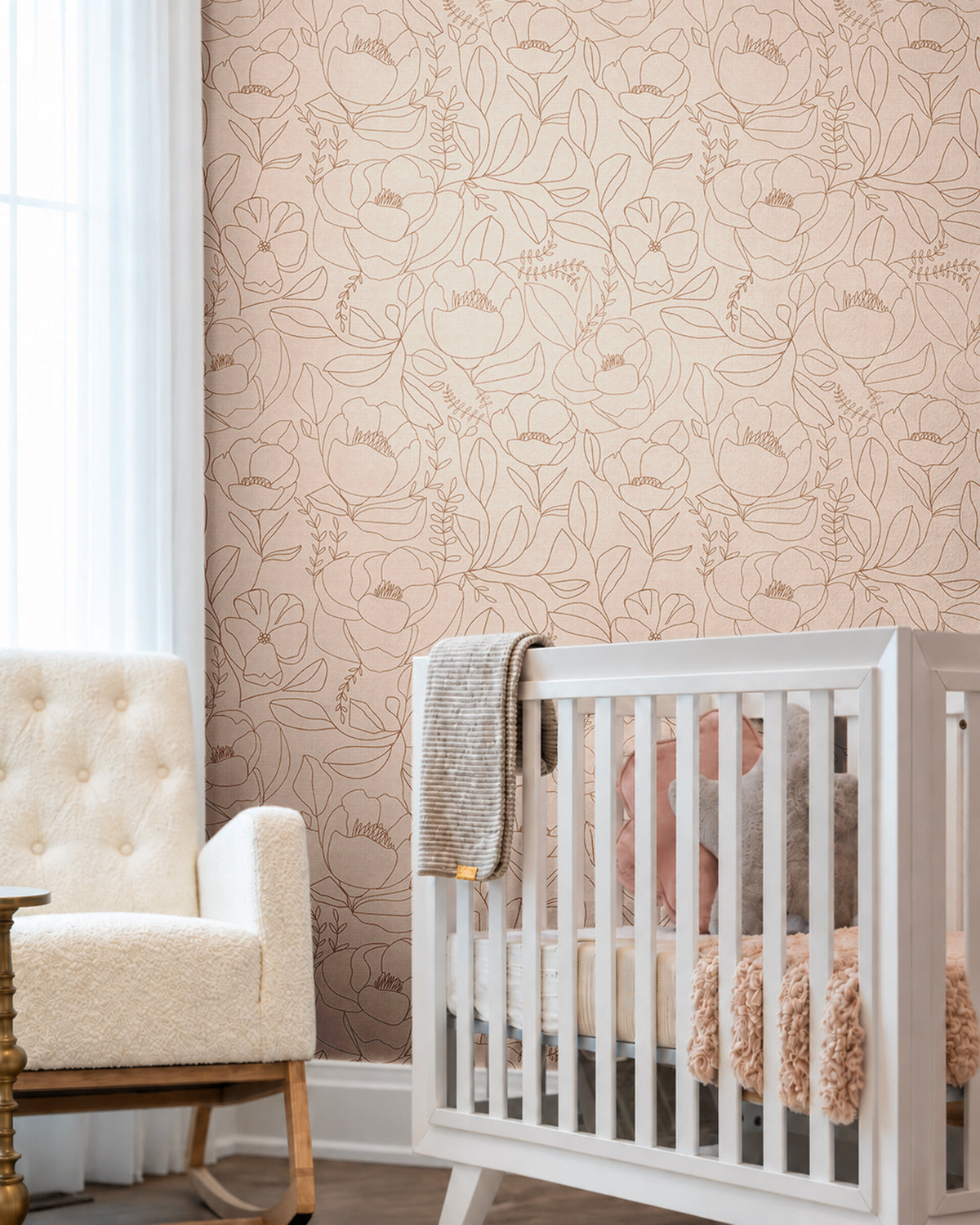 Open Bloom blush floral wallpaper in a neutral nursery with delicate brown line art flowers, white crib and upholstered