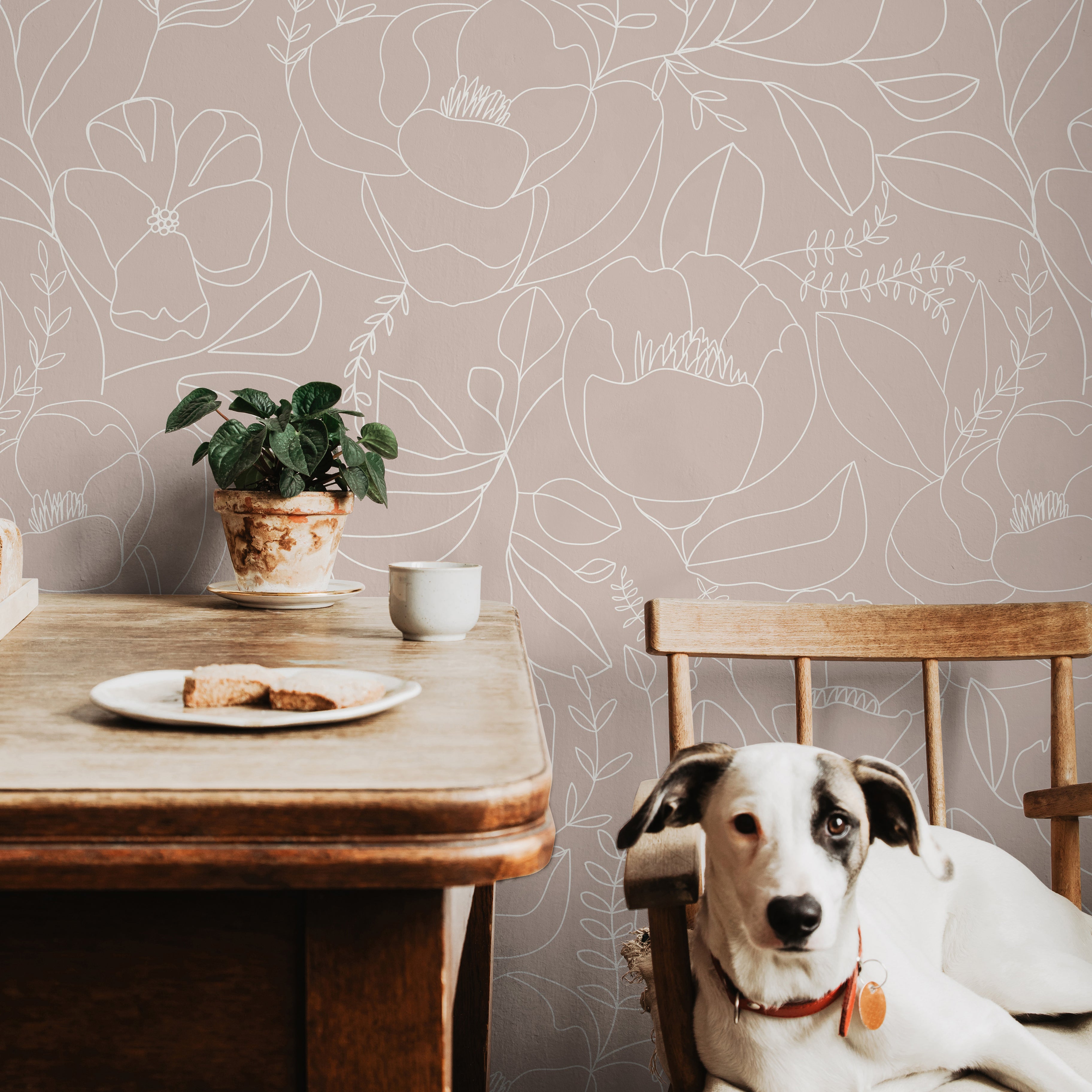 Dusty mauve pink botanical wallpaper with large white floral outlines styled in a soft dining room with natural wood accents.