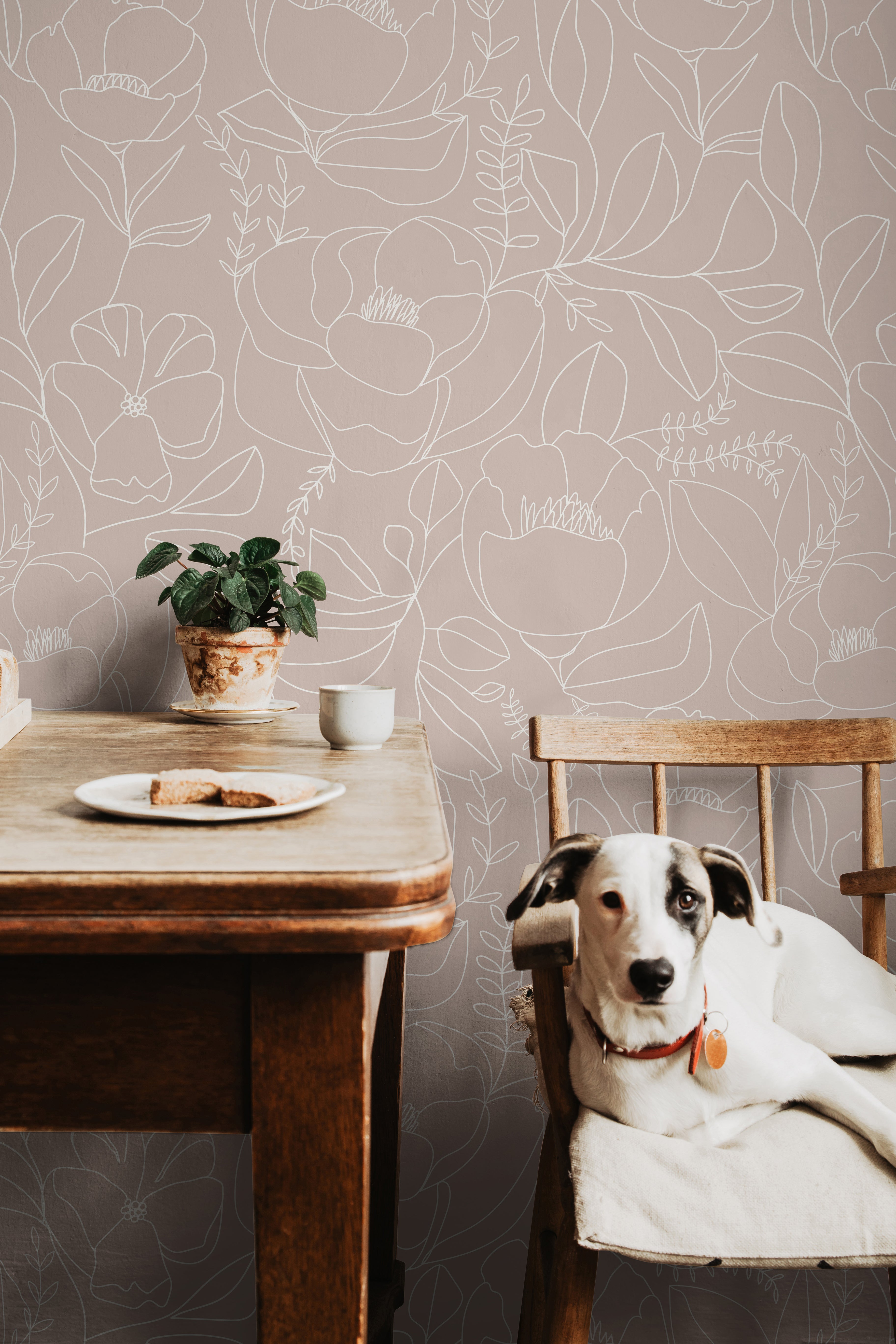 Dusty mauve pink botanical wallpaper with large white floral outlines styled in a soft dining room with natural wood accents.