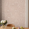 Open Bloom Tulle dusty mauve pink floral wallpaper with white botanical linework styled behind a wood table and chair.