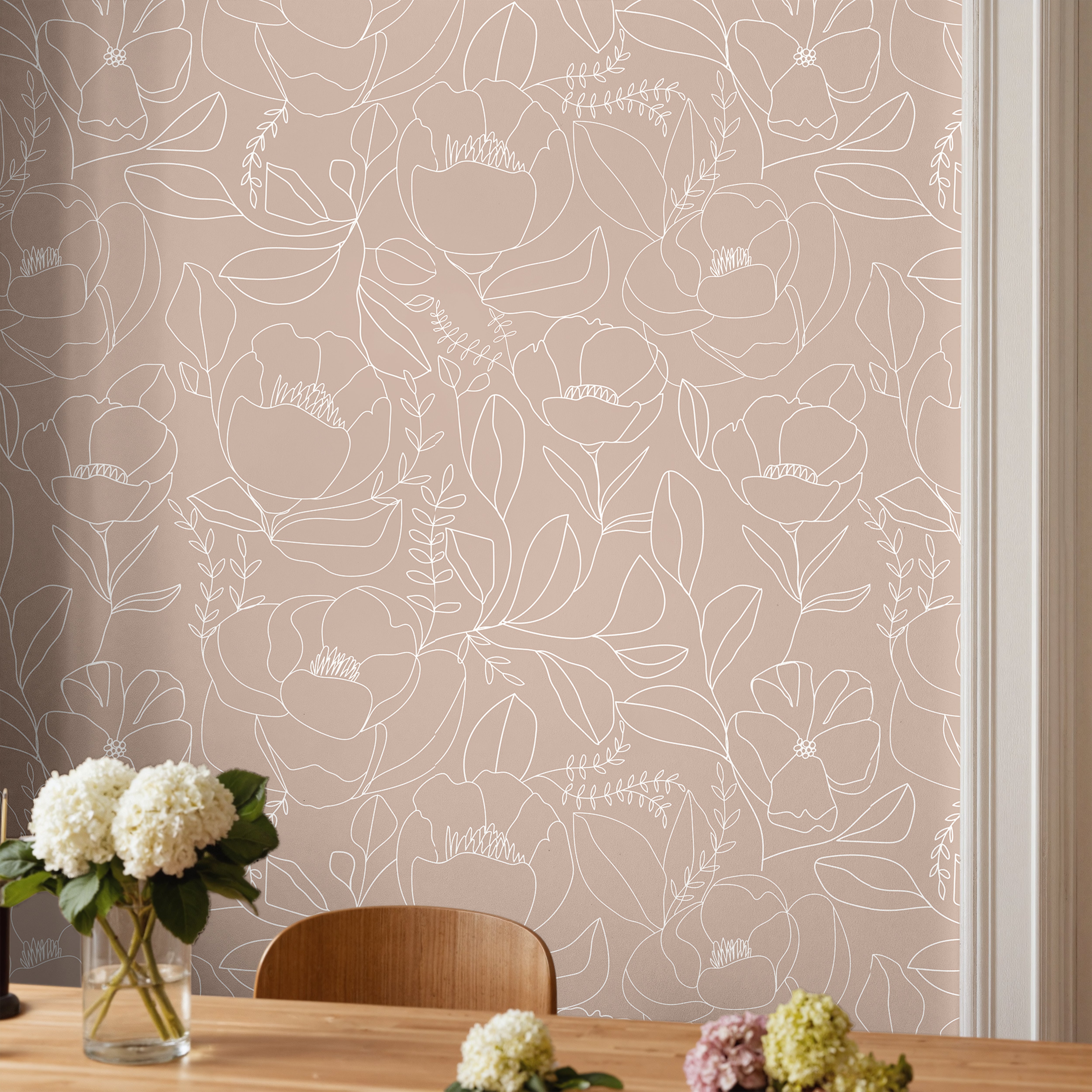 Open Bloom Tulle dusty mauve pink floral wallpaper with white botanical linework styled behind a wood table and chair.