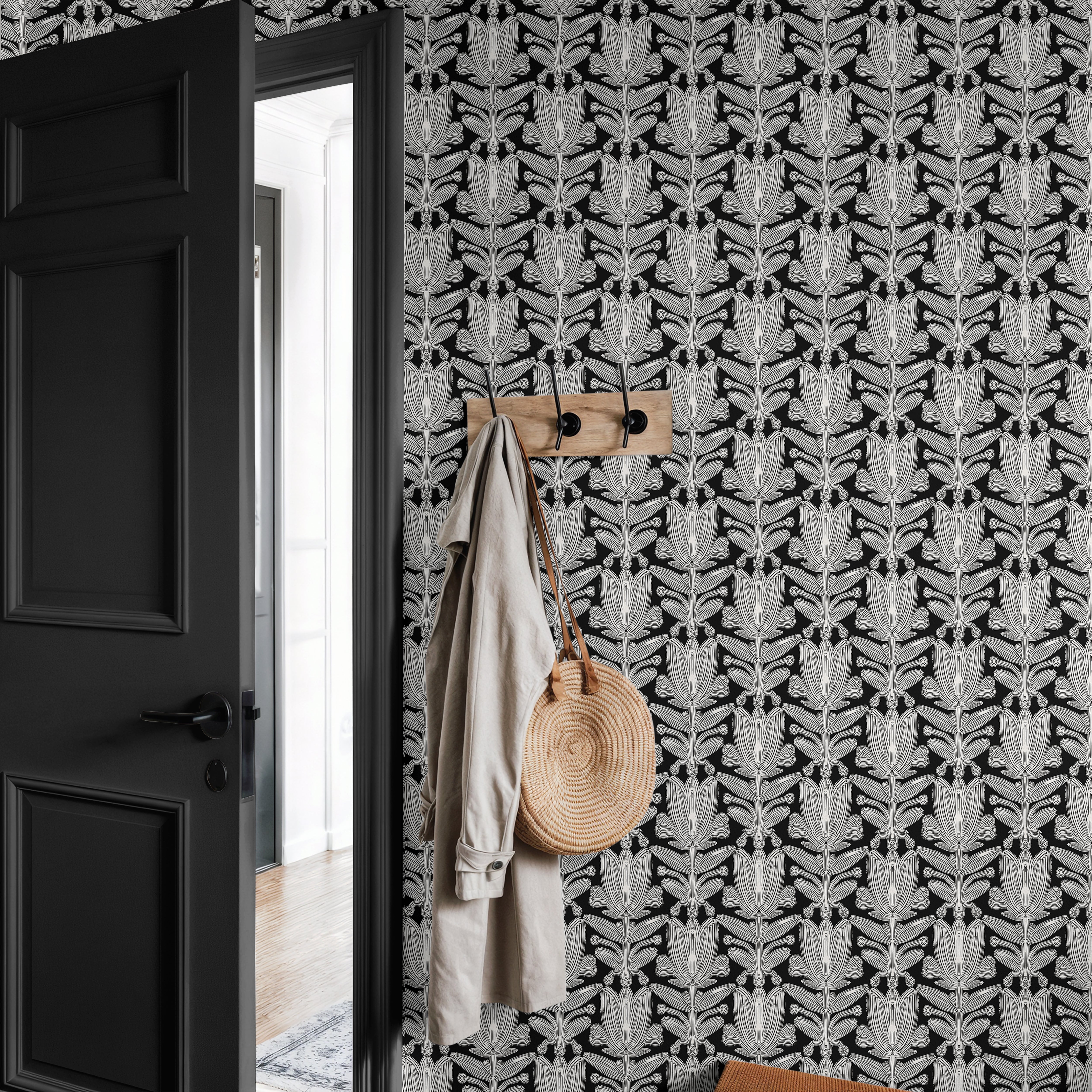 black and ivory floral wallpaper in entryway with black door wood hooks coat and woven bag