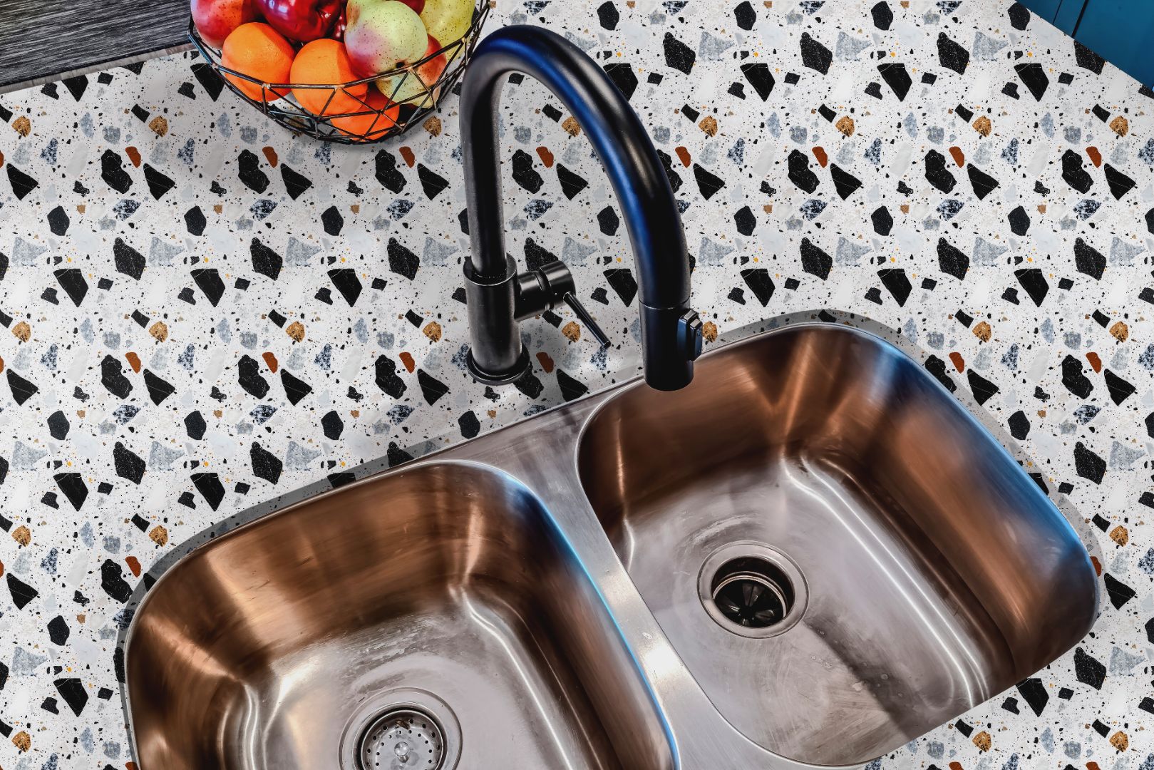 Shadow Terra Countertop Film applied around a stainless steel sink, showing terrazzo-inspired pattern with black, gray, and tan tones on a white background.
