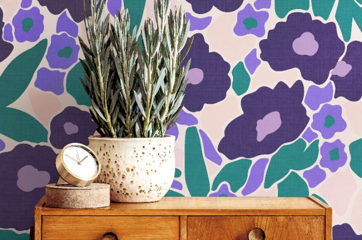 Wood sideboard and greenery complementing Violetta Bloom Wallpaper’s bold violet and teal floral pattern.