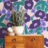 Wood sideboard and greenery complementing Violetta Bloom Wallpaper’s bold violet and teal floral pattern.