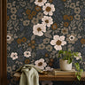 dark floral wallpaper with cream and amber flowers behind a wood bench with sage fabric and a potted plant
