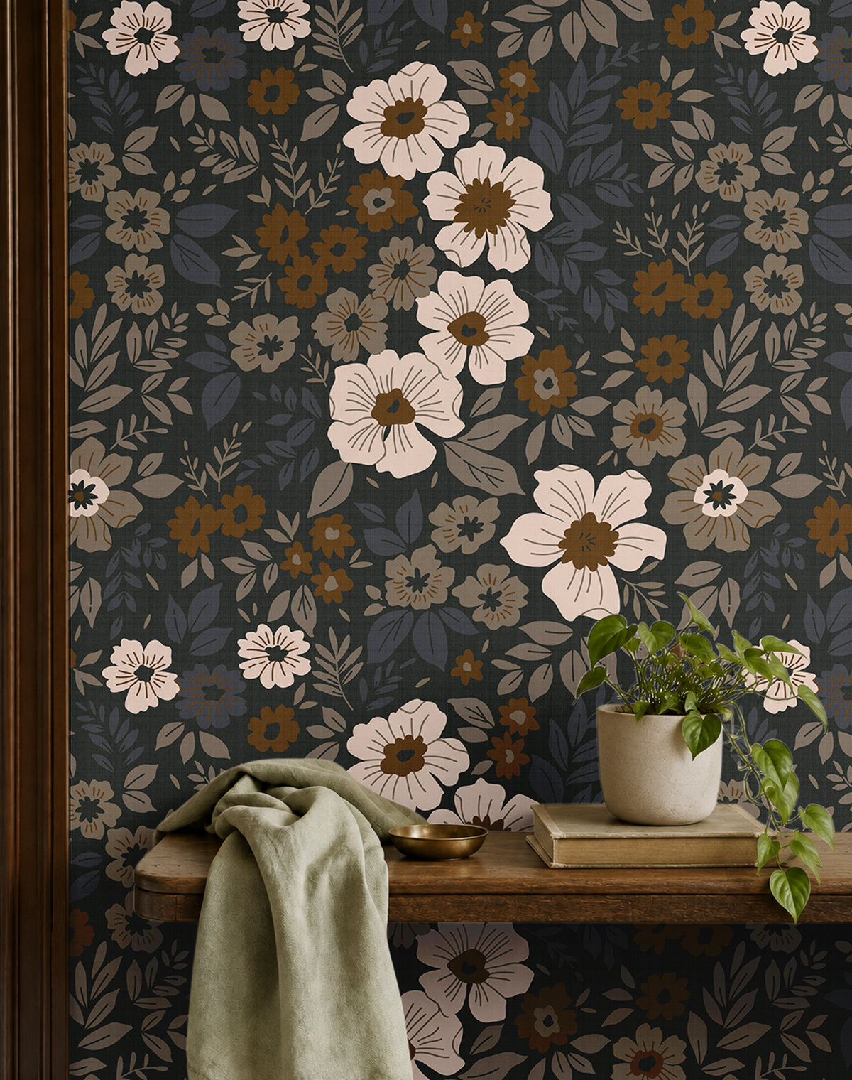 dark floral wallpaper with cream and amber flowers behind a wood bench with sage fabric and a potted plant
