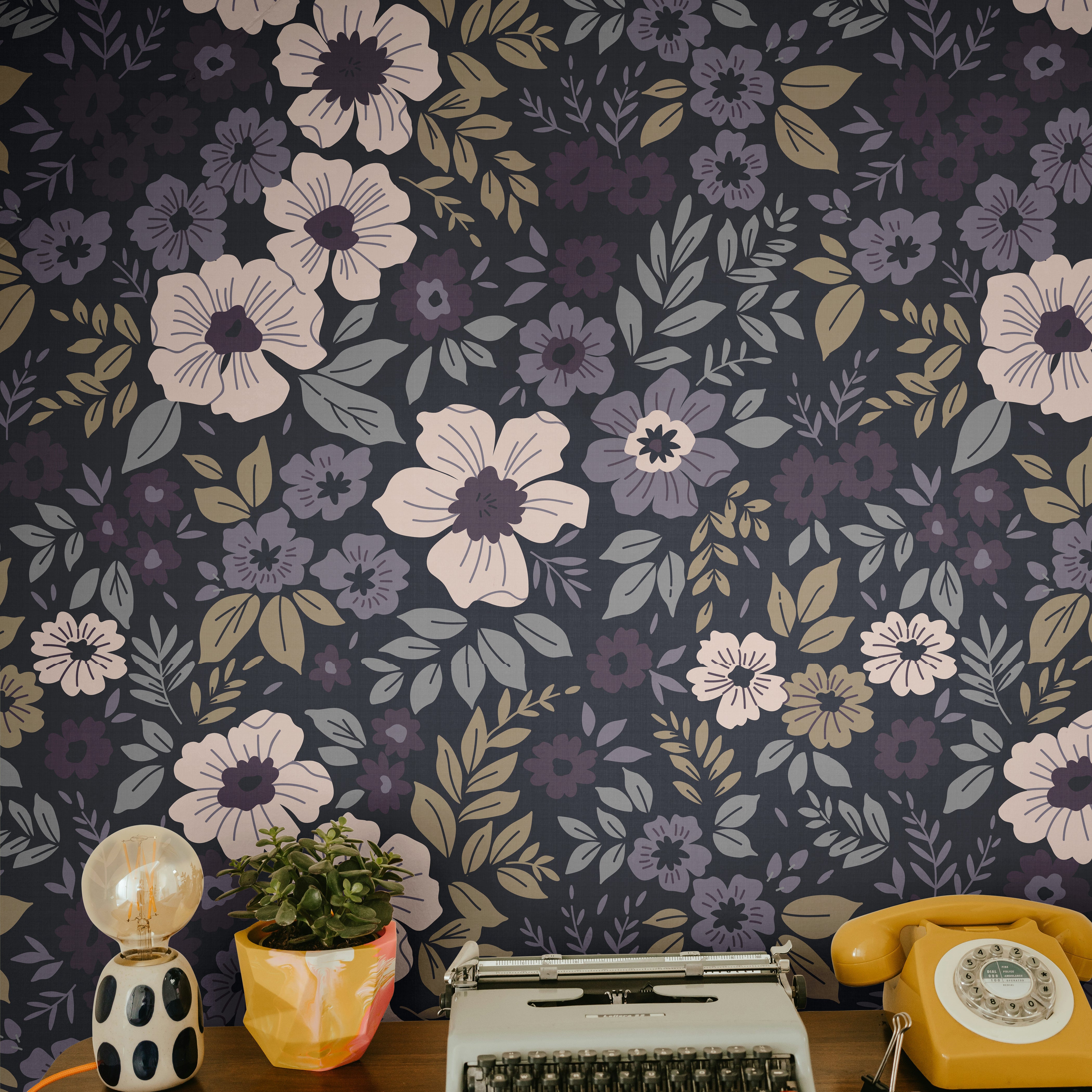 plum and lilac floral wallpaper behind a wood desk with a typewriter yellow phone and potted plant