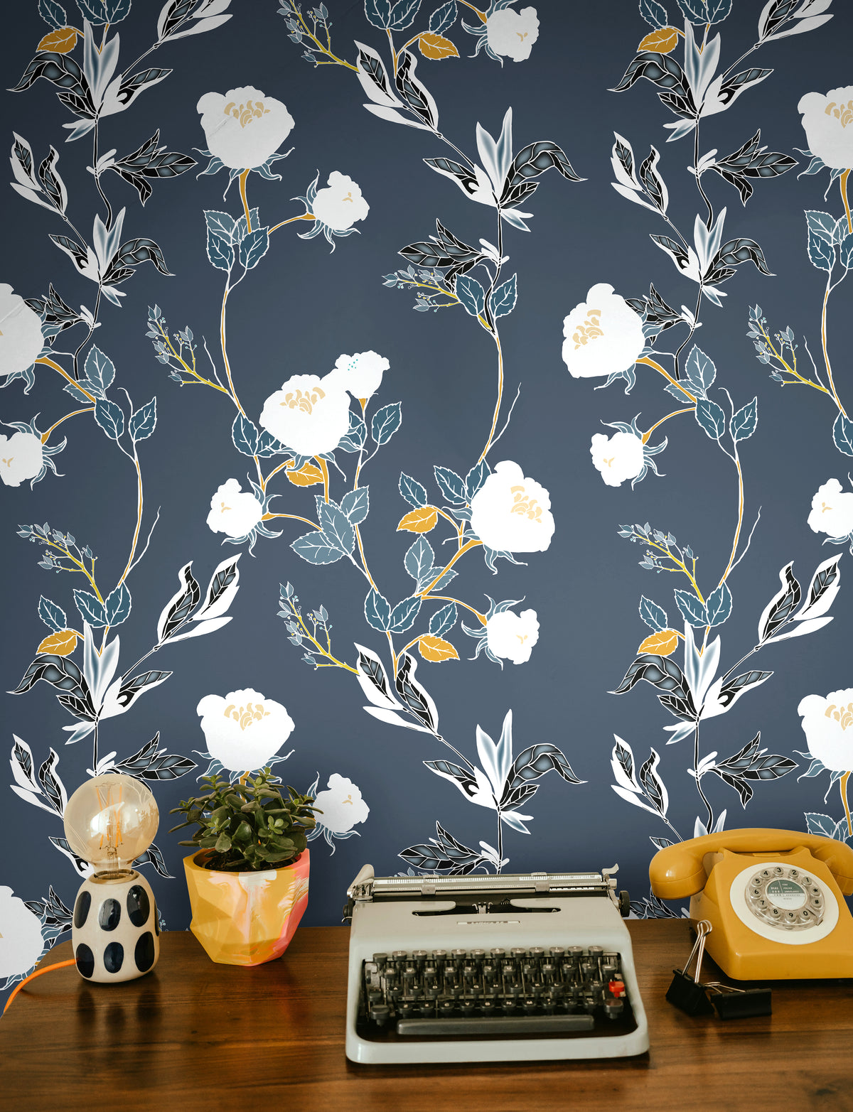 white florals with green and orange stems on lighter navy background behind eclectic desk interior