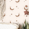 Wallpaper 3844: Neutral boho nursery wallpaper featuring soft brown crescent moons and minimalist starbursts on a cream background, styled above a woven changing basket with natural accents.