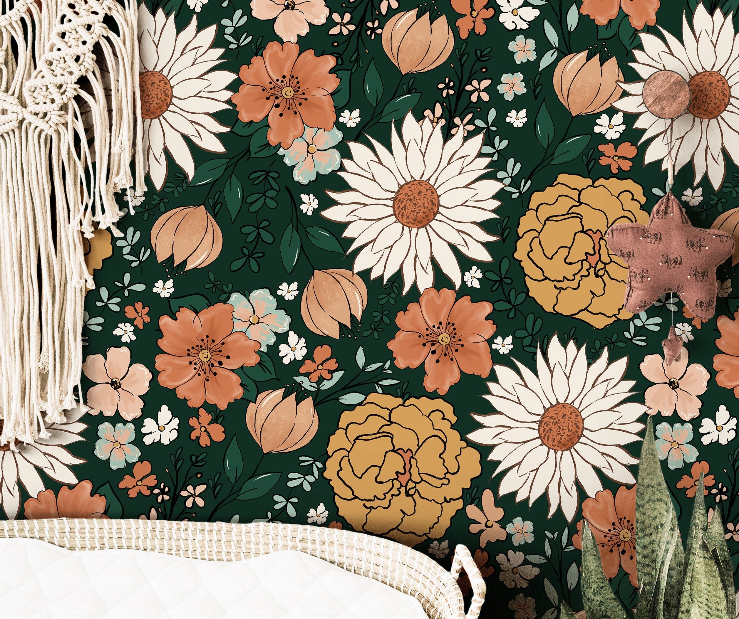 Wallpaper 137: Wallpaper with a bold floral pattern featuring oversized daisies, marigolds, cosmos, and wildflowers in rust, mustard, blush, and cream tones on a deep green background, styled above a rattan changing basket in a boho nursery.


