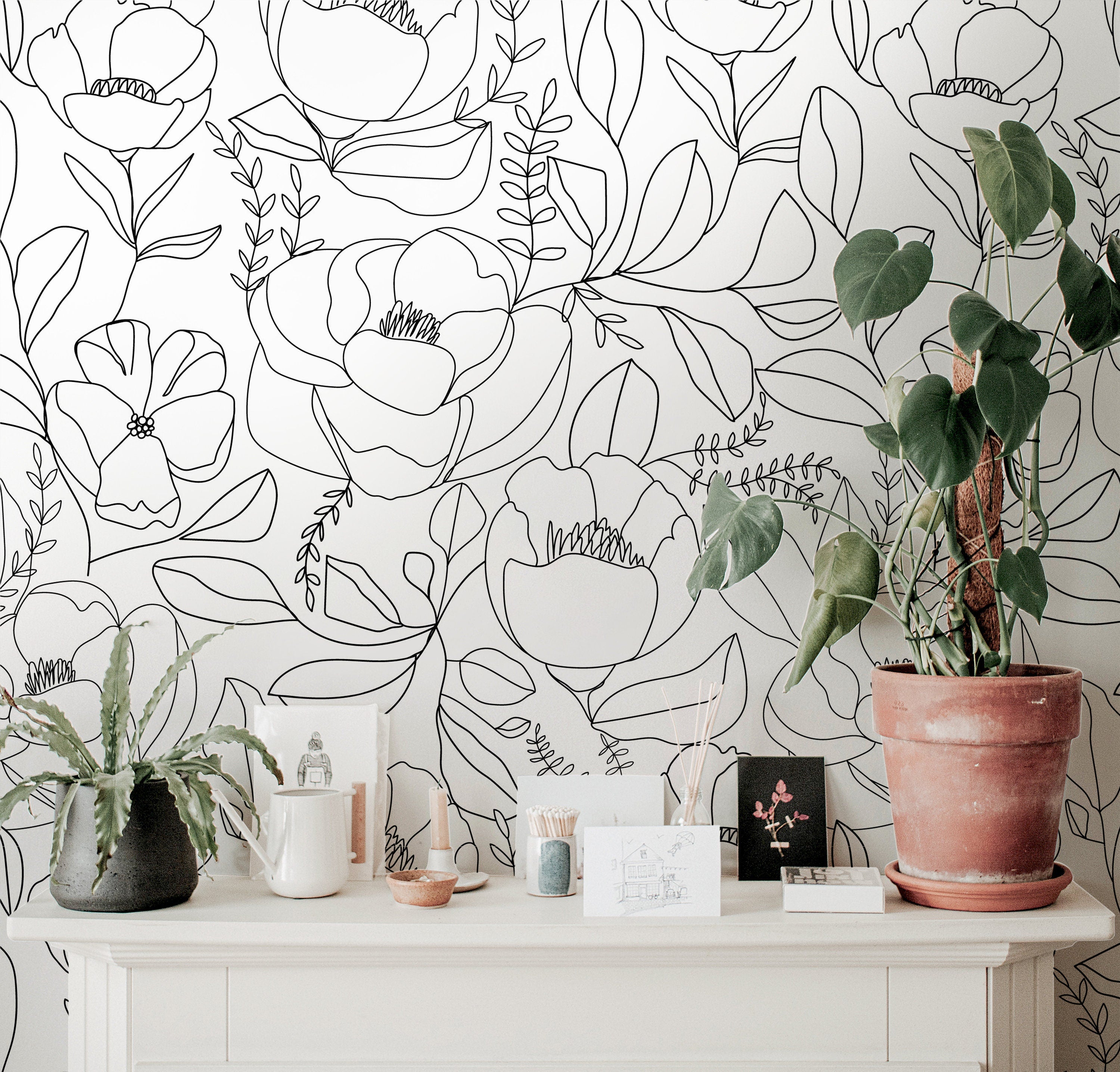 Wallpaper 646a: Minimalist floral wallpaper in black line art on a soft white background, styled with natural-toned decor and potted plants atop a modern cream console.