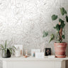 Wallpaper 915: Neutral-toned wallpaper featuring large-scale line art floral outlines in taupe on a cream background, styled with indoor plants and delicate pottery on a white console.