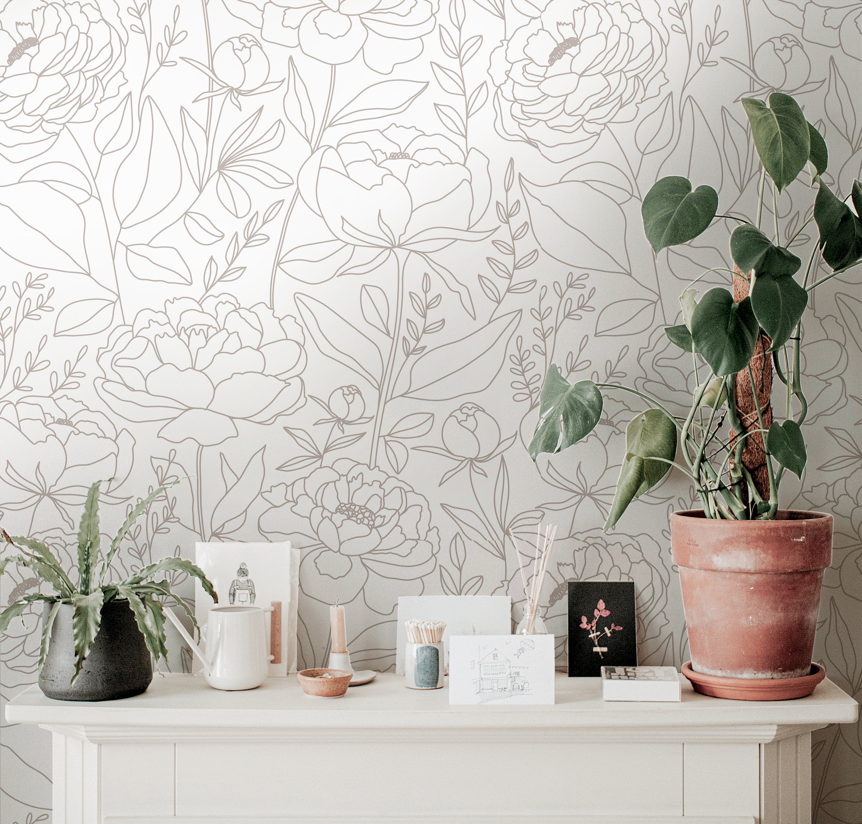 Wallpaper 915: Neutral-toned wallpaper featuring large-scale line art floral outlines in taupe on a cream background, styled with indoor plants and delicate pottery on a white console.