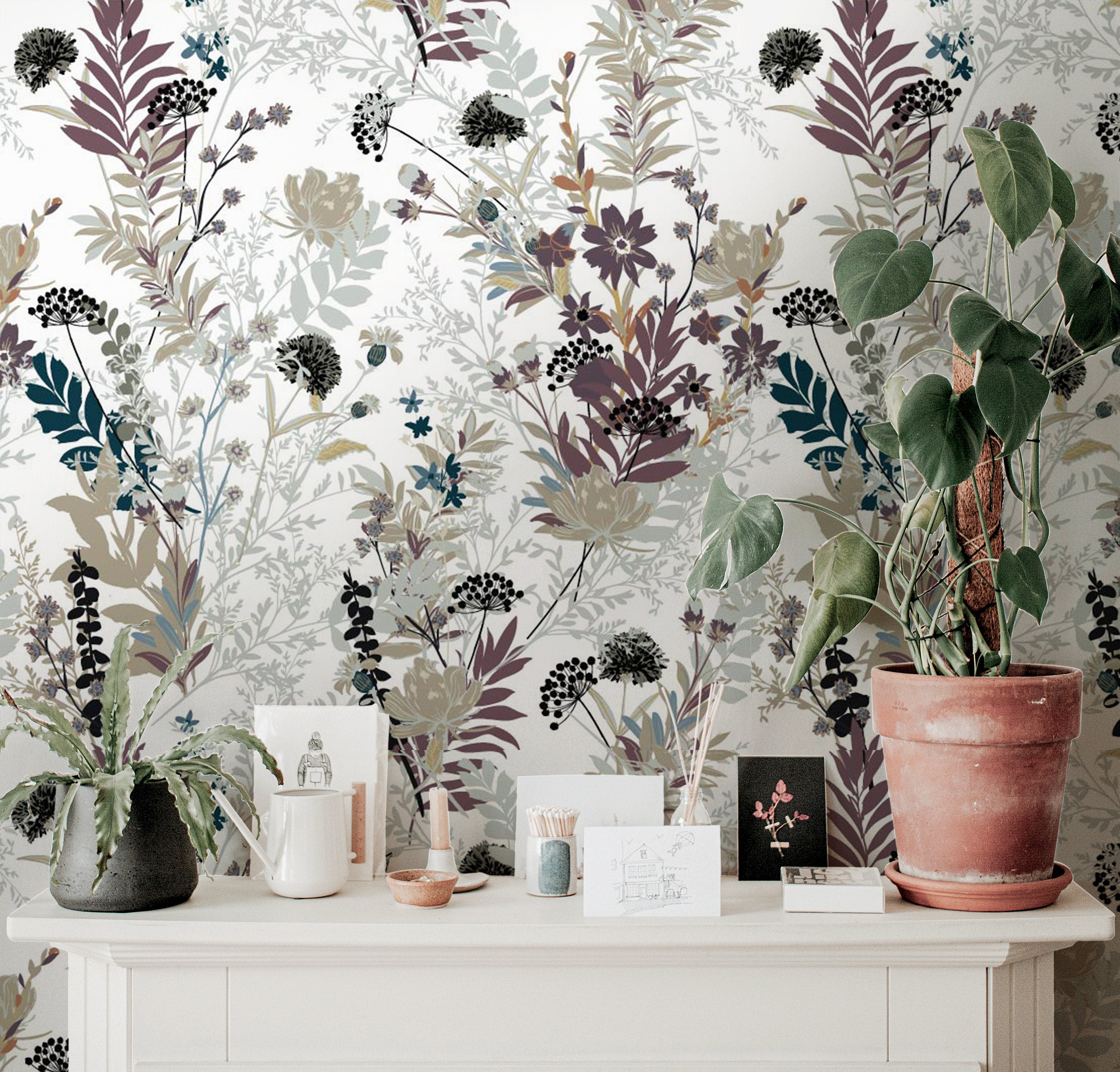 Wallpaper 917: Soft botanical wallpaper with a delicate floral and foliage design in muted tones of lavender, sage, and beige behind a white mantle decorated with houseplants and art prints.