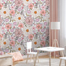 Wallpaper 555a: A bright and charming children's room with soft pink floral wallpaper featuring delicate daisies, peonies, and garden blooms, complemented by pastel decor and natural wood furniture.